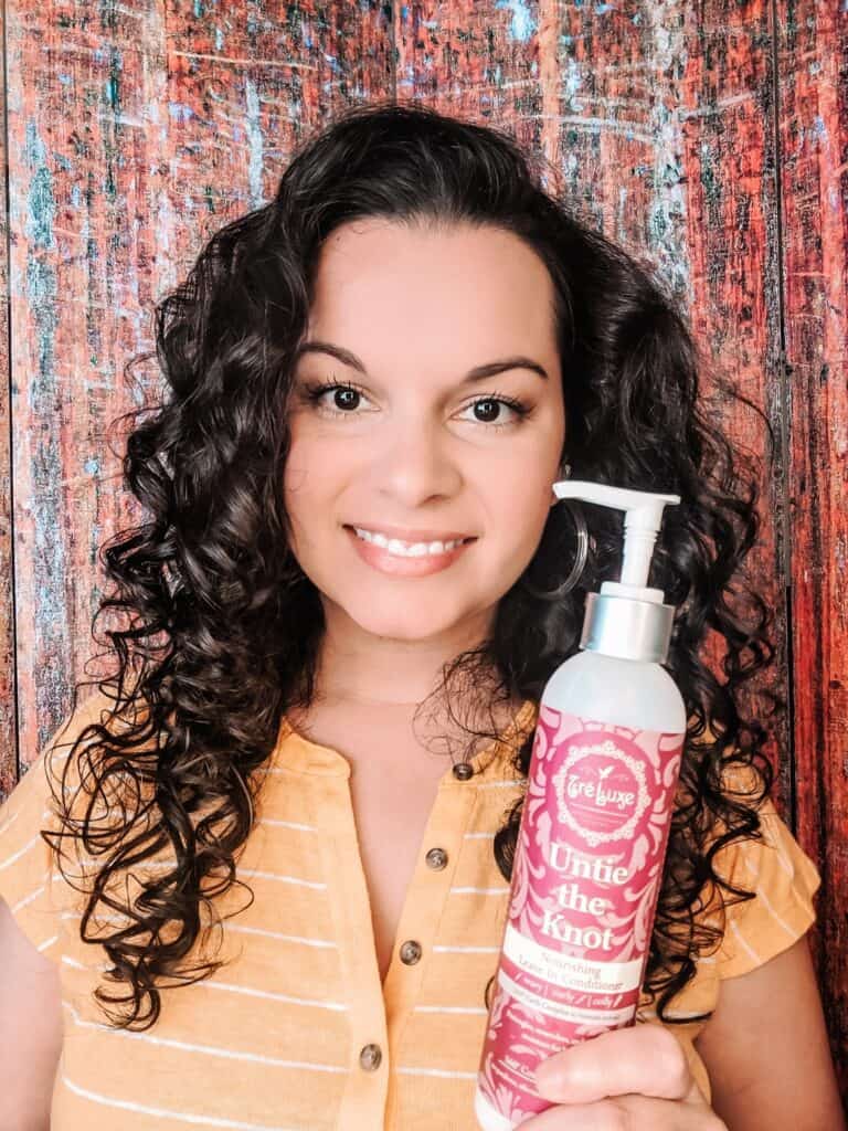 holding up the TreLuxe conditioner for curly hair showing my styled curls. This is a curly girl method approved leave-in conditioner.