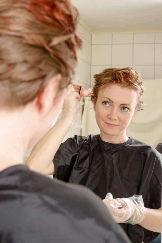 woman fixes orange hair with box dye at home, looking in mirror as she dyes her hair